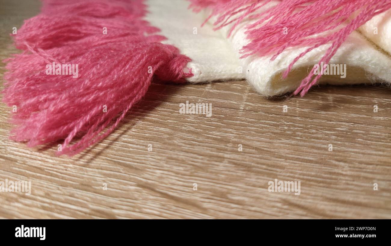 Bufanda hecha de hilos blancos y rosados. Knitwork en una mesa de madera. Espacio vacío para el texto. Colores pastel suaves. Ropa de invierno. Foto de stock