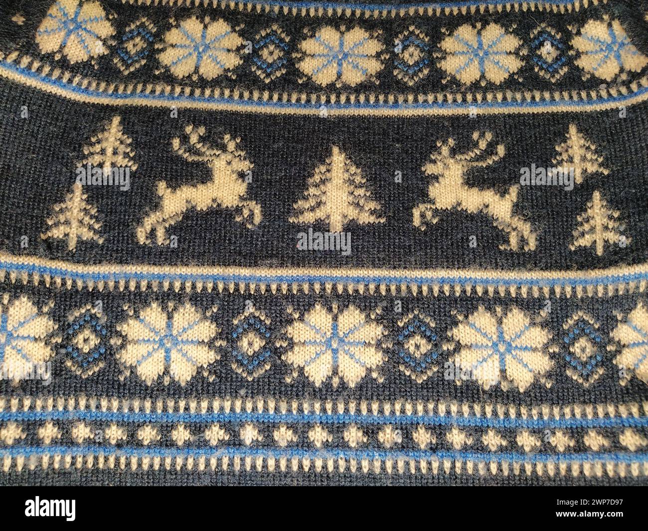 Un fragmento de un adorno en un suéter de poliéster o lana de punto. Motivos de invierno. Hilos azules para tejer a mano. Hilo blanco tejido patrón. Flujo Foto de stock