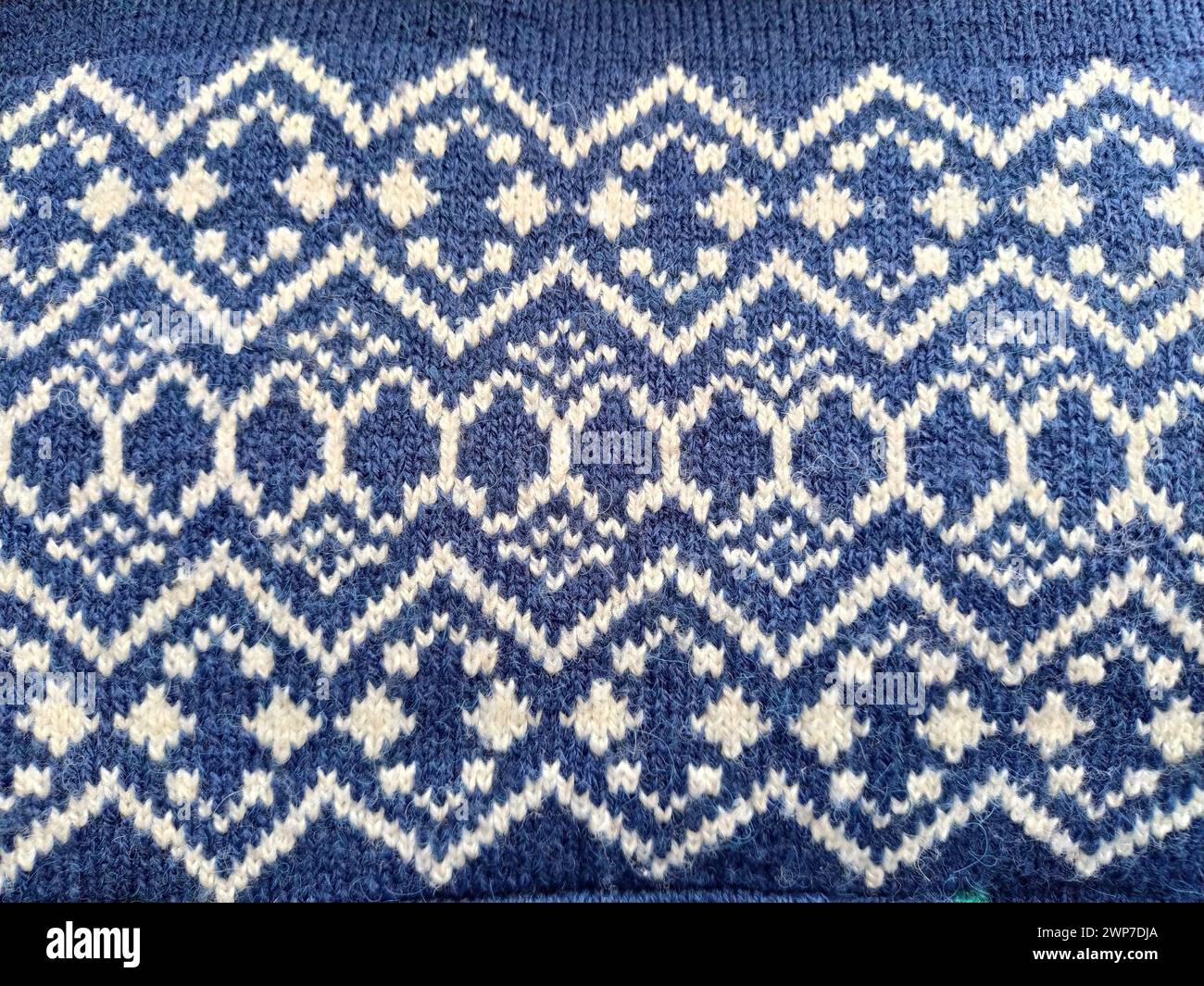 Un fragmento de un adorno en un suéter de poliéster o lana de punto. Motivos de invierno. Hilos azules para tejer a mano. Patrón de punto de una threa blanca Foto de stock