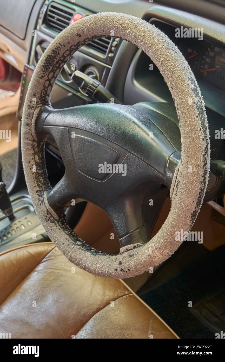 vieja cubierta desgastada del volante del coche, se desvaneció de la exposición a la luz solar y peló el cuero de uso constante durante mucho tiempo, enfoque selectivo Foto de stock