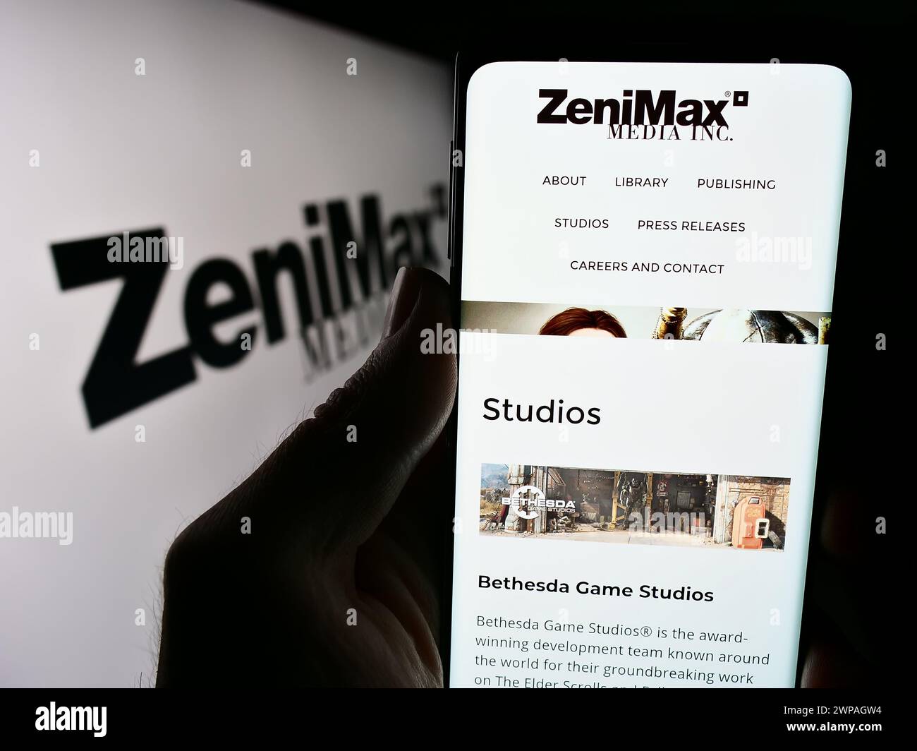 Persona que sostiene el smartphone con el sitio web de la compañía de videojuegos de EE.UU. ZeniMax Media Inc. Frente al logotipo del negocio. Enfoque en el centro de la pantalla del teléfono. Foto de stock