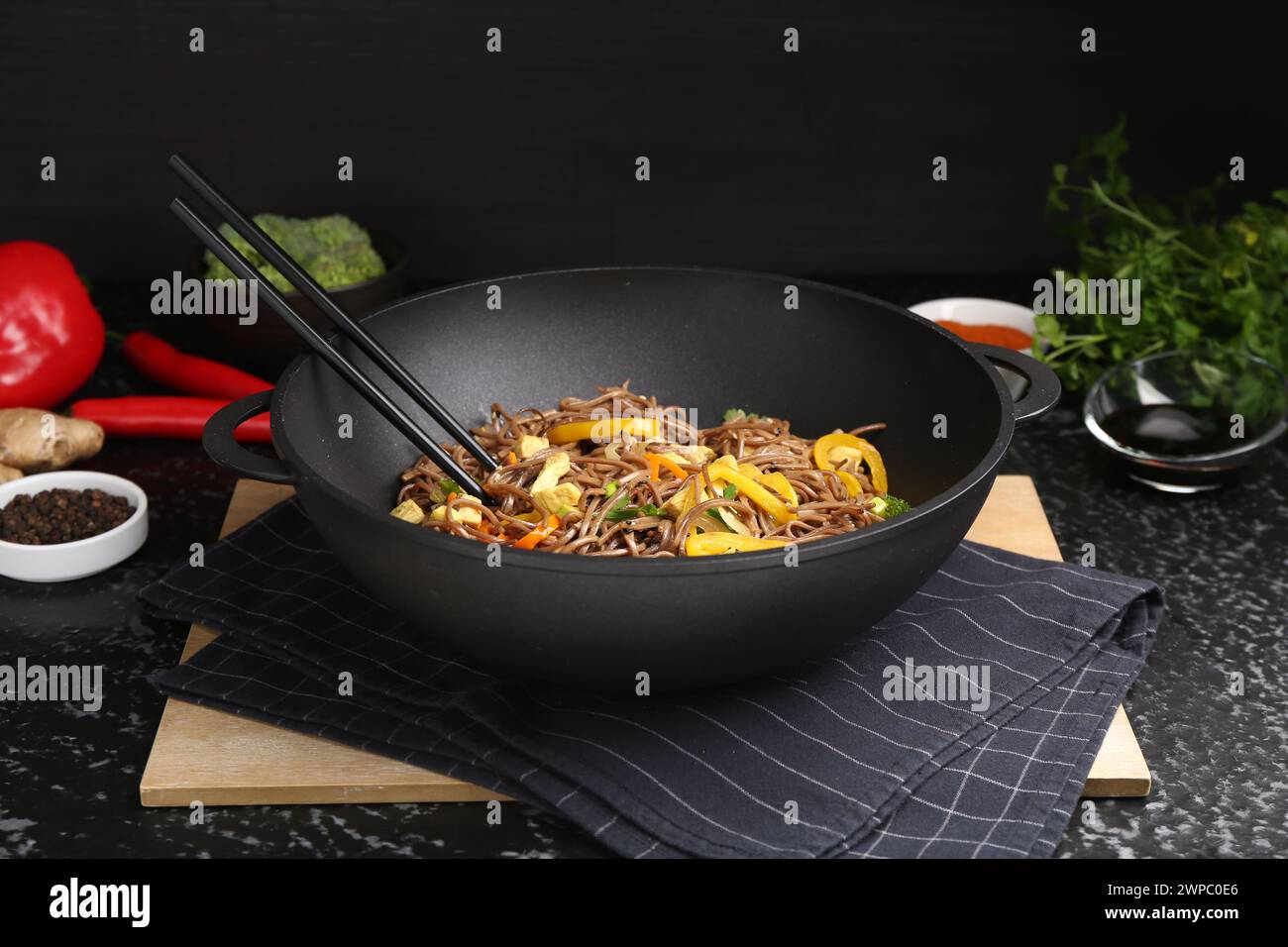 Salteado. Sabrosos fideos con verduras, carne y palillos en wok sobre mesa de textura oscura Foto de stock