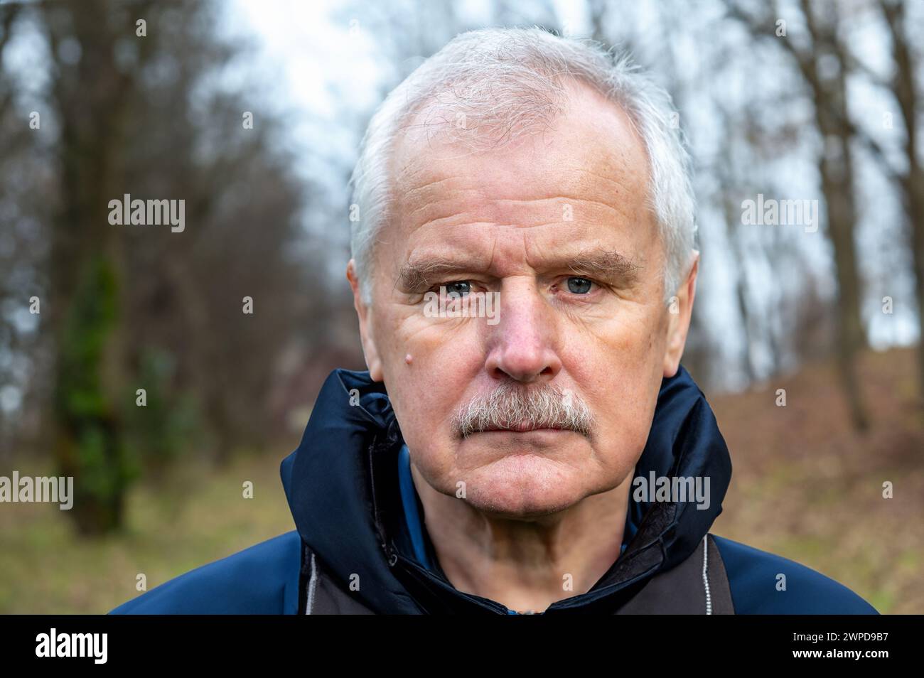 El ciudadano mayor durante una caminata en el bosque mira seriamente a la cámara. Símbolo para personas mayores que permanecen activas. Foto de stock