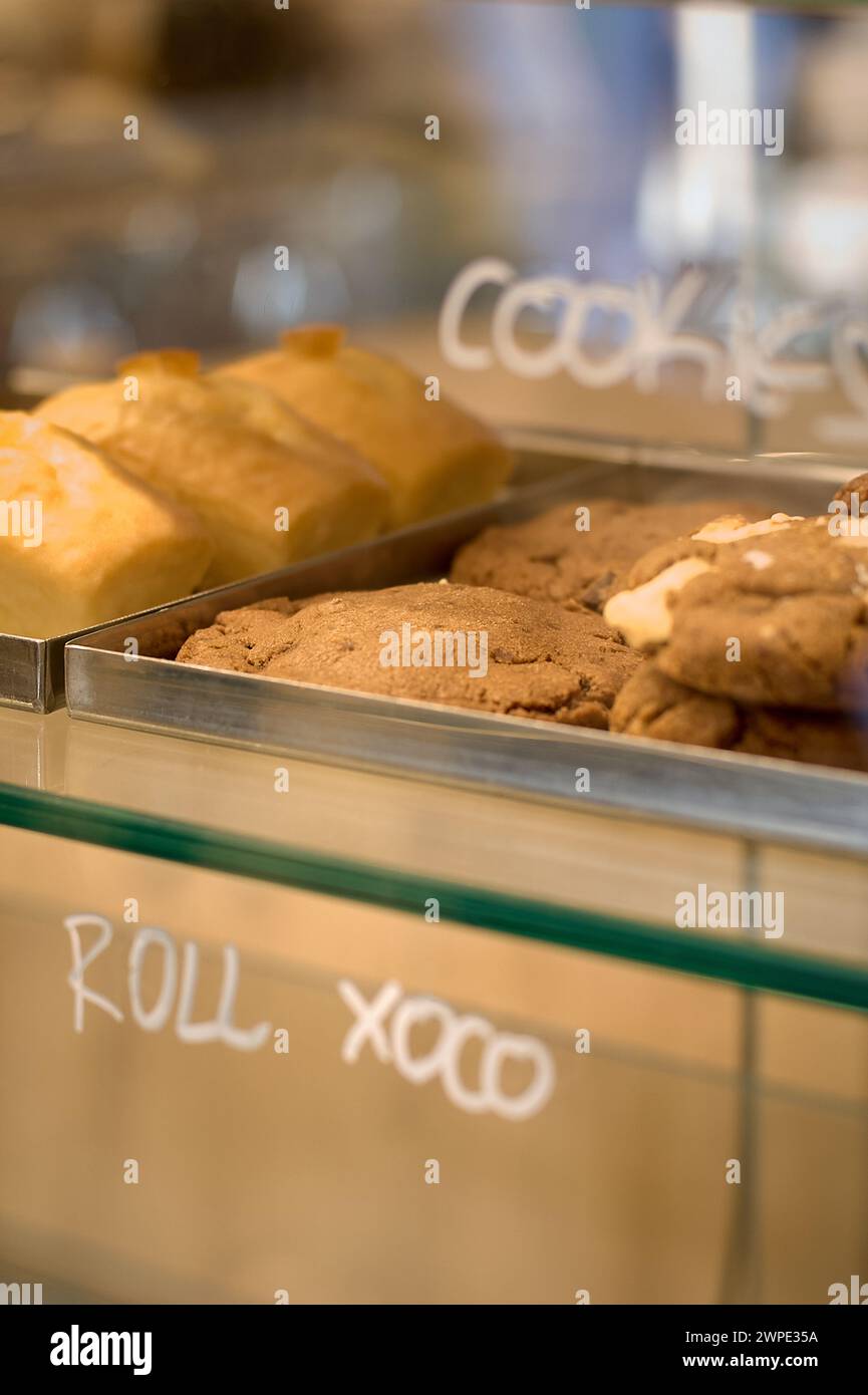 Vitrina con una variedad de pasteles y galletas, etiquetadas, en una pastelería iluminada. Foto de stock