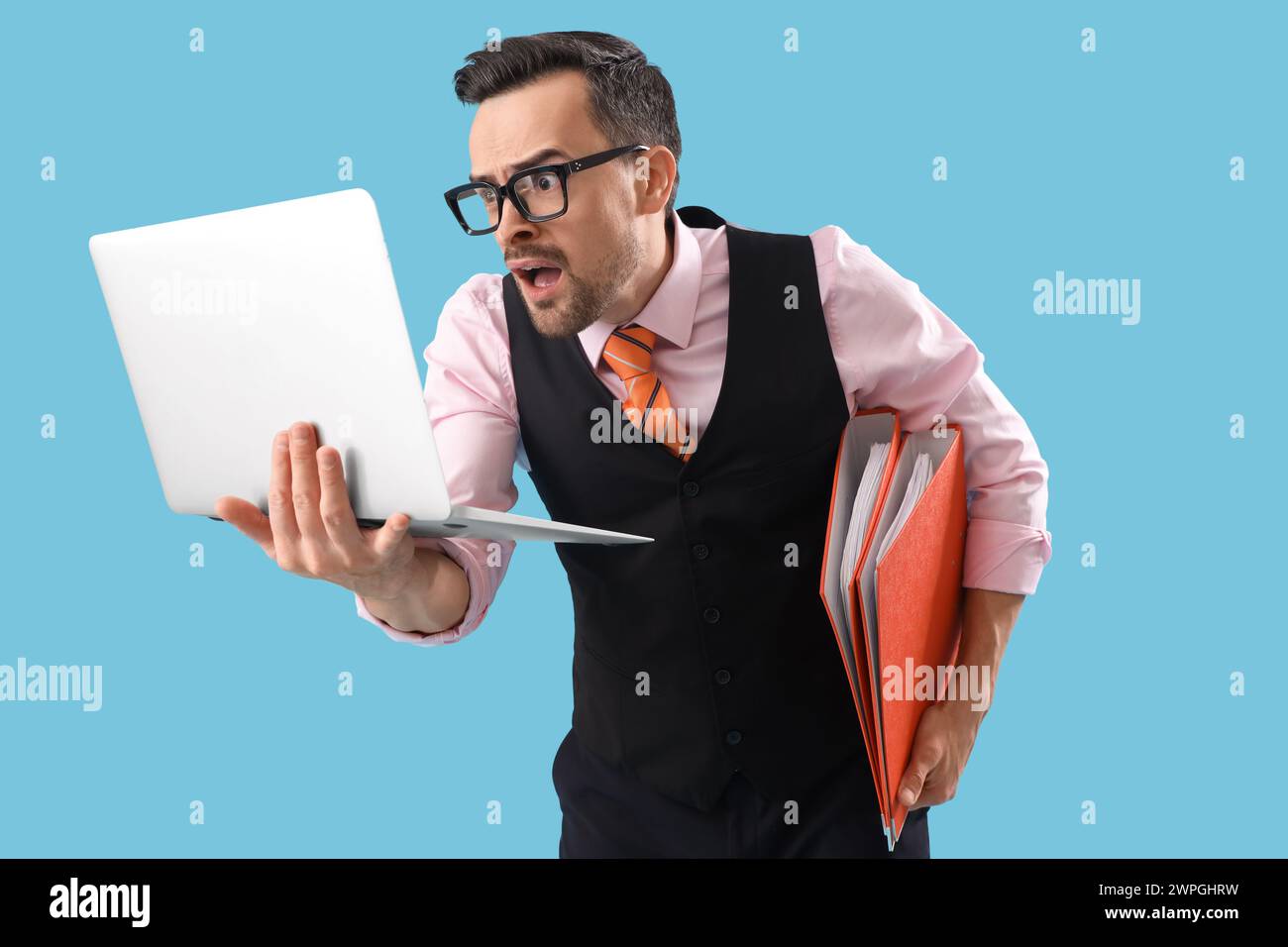Divertido hombre de negocios sorprendido con carpetas y ordenador portátil sobre fondo azul Foto de stock