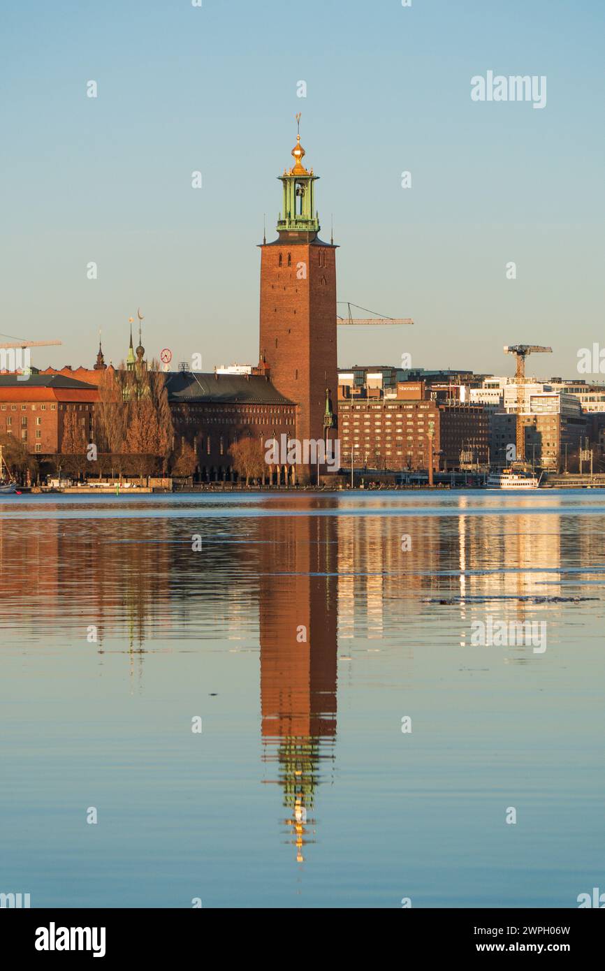 El ayuntamiento, edificio del ayuntamiento de Estocolmo, en Kungsholmen, reflejos en el lago, al atardecer, cielo azul claro, finales del invierno. Famoso punto de referencia de SW Foto de stock