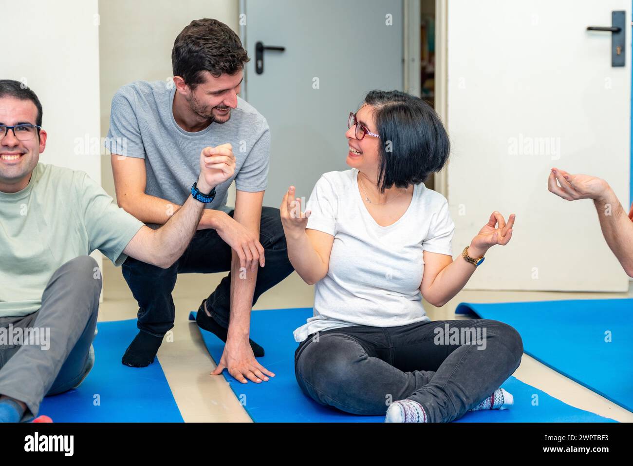 Instructor de yoga hablando con una mujer adulta discapacitada feliz sentada en una esterilla durante la clase de yoga Foto de stock
