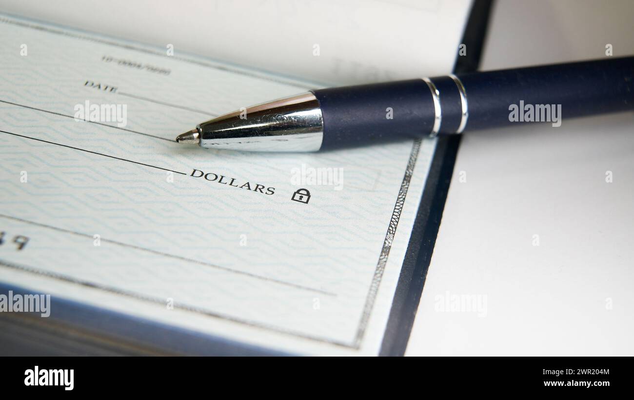 Un bolígrafo azul está listo en un cheque en blanco con su punta descansando cerca de la línea de pago, listo para que alguien llene los detalles necesarios Foto de stock