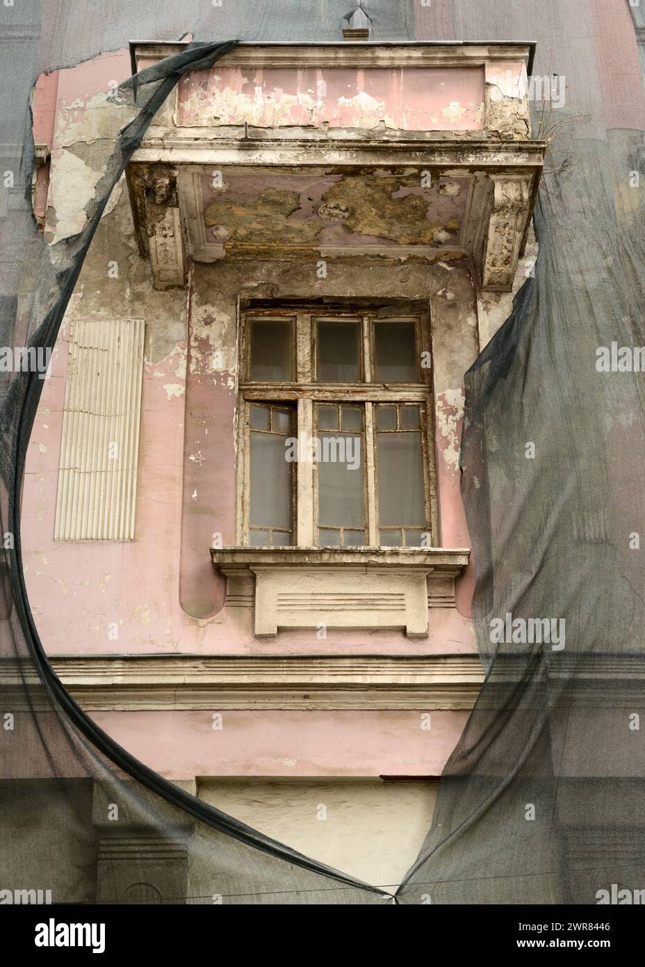 Balcón y ventana abandonados en la fachada del edificio rosa con malla de seguridad Foto de stock