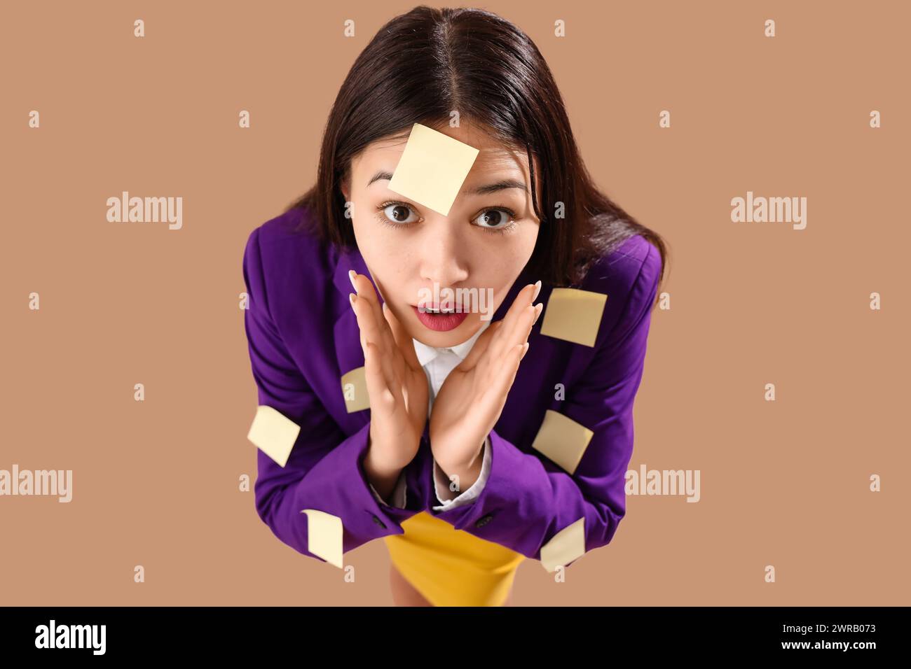 Divertida empresaria asiática sorprendida con notas pegajosas sobre fondo marrón Foto de stock