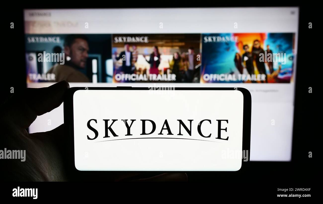 Persona que sostiene el teléfono móvil con el logotipo de la compañía de producción de películas americana Skydance Media LLC en frente de la página web. Enfoque en la pantalla del teléfono. Foto de stock