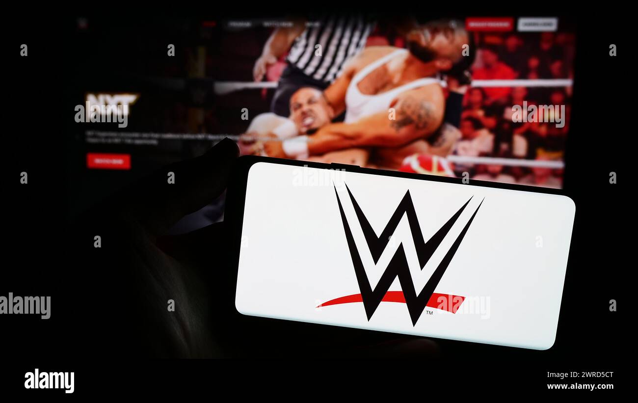 Persona que sostiene el smartphone con el logotipo de la empresa de promoción World Wrestling Entertainment (WWE) delante del sitio web. Enfoque en la pantalla del teléfono. Foto de stock