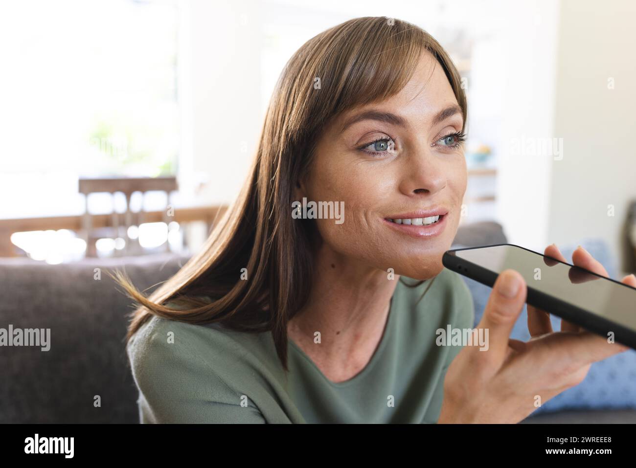 Mujer caucásica habla en un teléfono inteligente, su cabello castaño enmarcando su cara sonriente Foto de stock