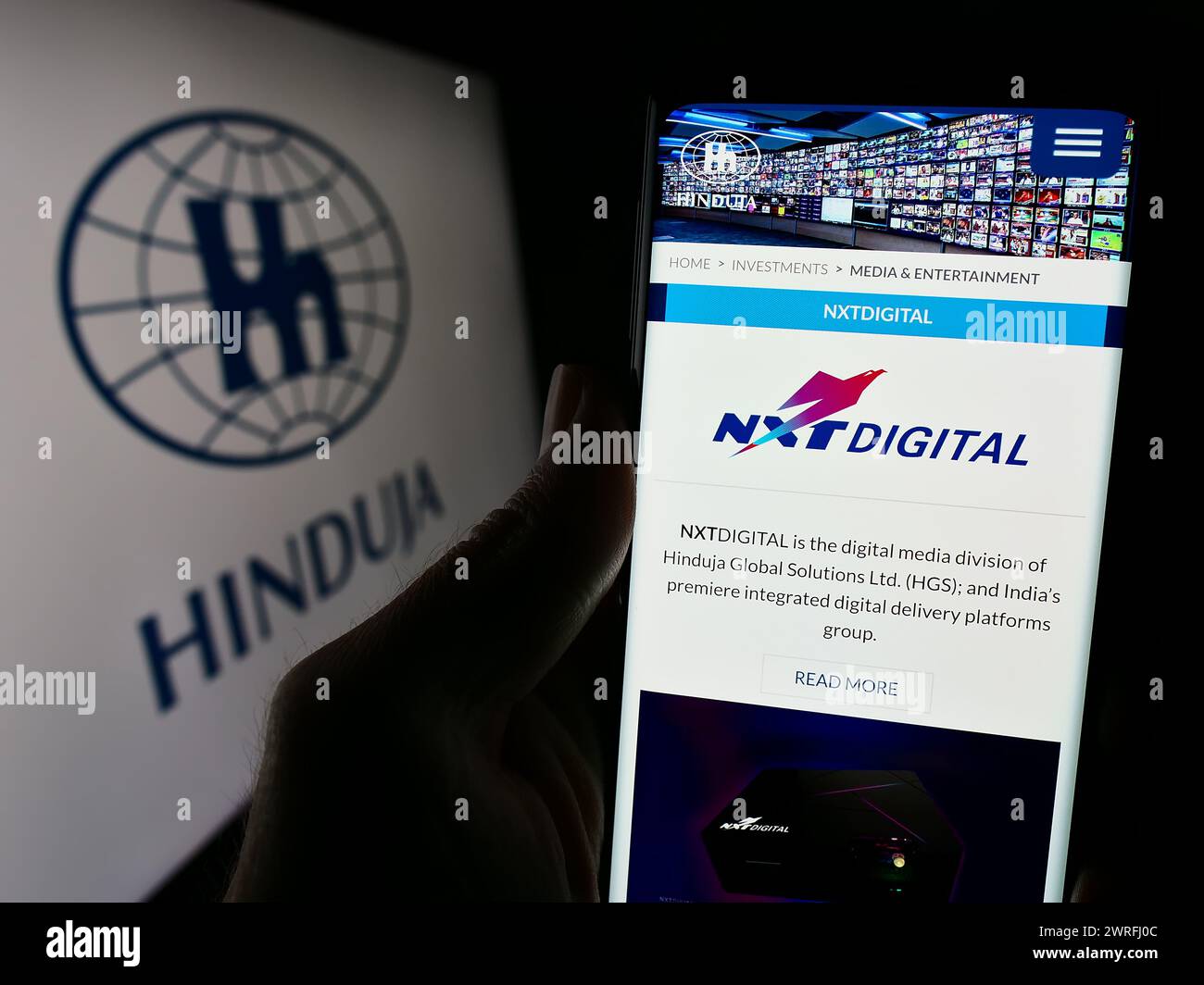 Persona que sostiene el teléfono celular con la página web del conglomerado indio Hinduja Group Ltd. Delante del logotipo del negocio. Enfoque en el centro de la pantalla del teléfono. Foto de stock