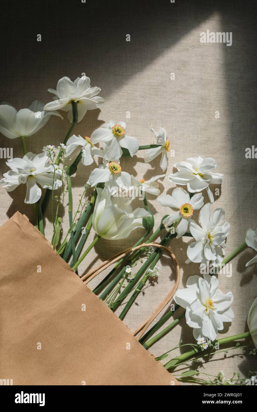 Vista aérea de un montón de narcisos blancos y tulipanes en una bolsa de papel sobre una mesa a la luz del sol Foto de stock