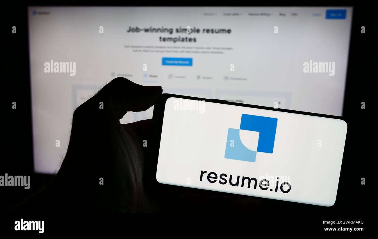 Persona que sostiene el smartphone con el logotipo de la empresa creadora de currículum holandés Resume.io en frente del sitio web. Enfoque en la pantalla del teléfono. Foto de stock