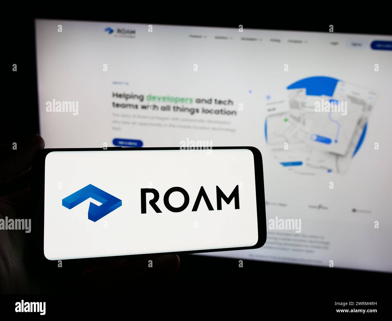 Persona que sostiene el smartphone con el logotipo de la compañía holandesa de seguimiento de la ubicación Roam.ai delante del sitio web. Enfoque en la pantalla del teléfono. Foto de stock