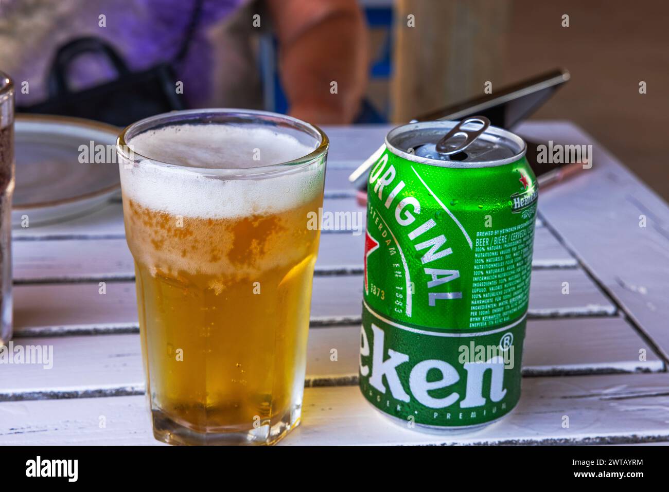 Vista de cerca de un vaso lleno de cerveza fría y lata de cerveza Heineken de pie sobre una mesa de madera. Foto de stock