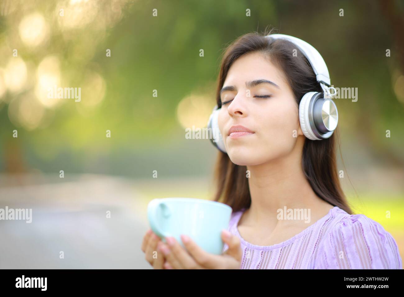 Mujer relajada con auriculares meditando sosteniendo taza de té en un parque Foto de stock