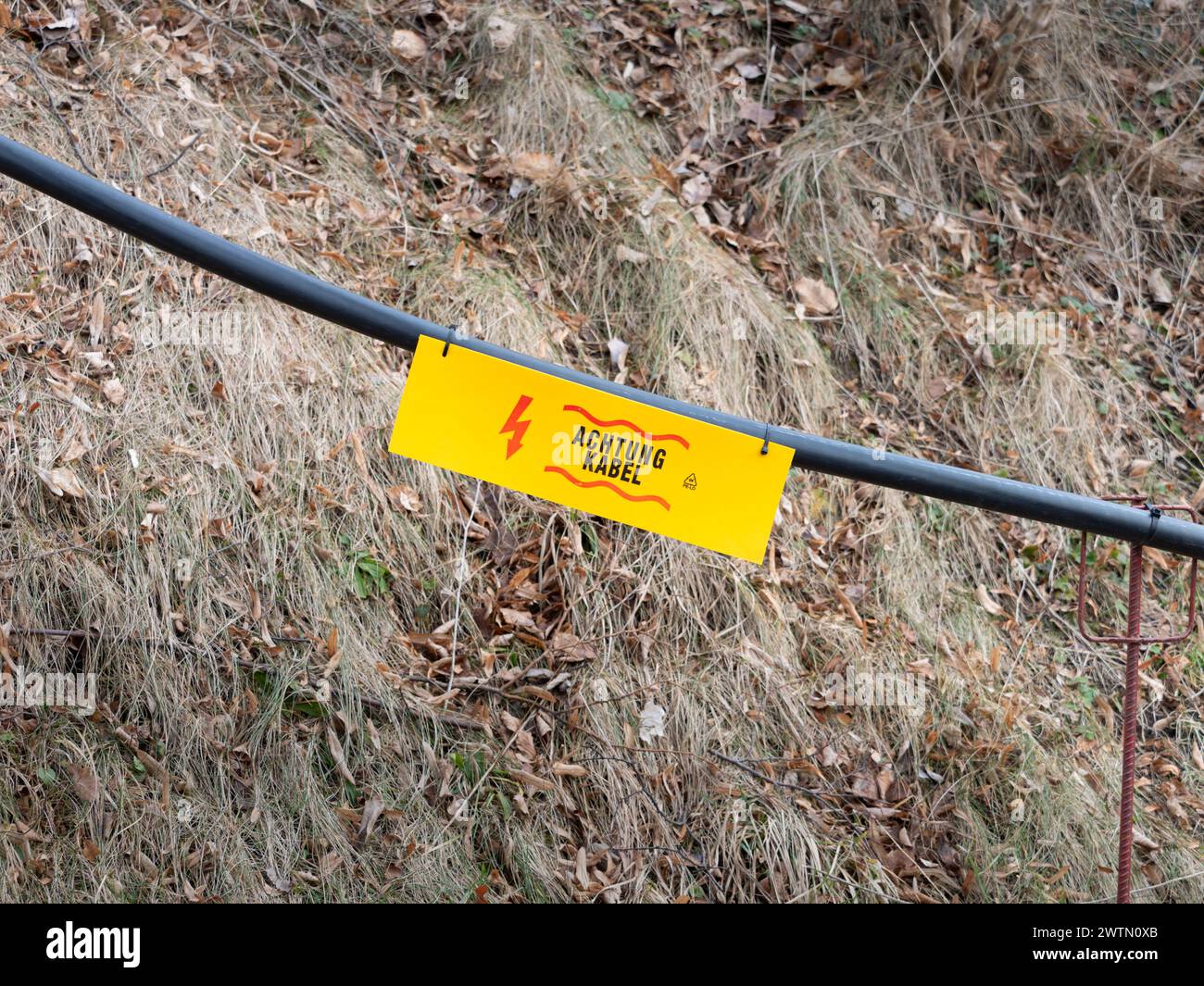 Achtung Kabel (Cable Eléctrico de Precaución) firma en un grueso cable de suministro negro. Seguridad en un sitio de construcción frente a una propiedad. Foto de stock