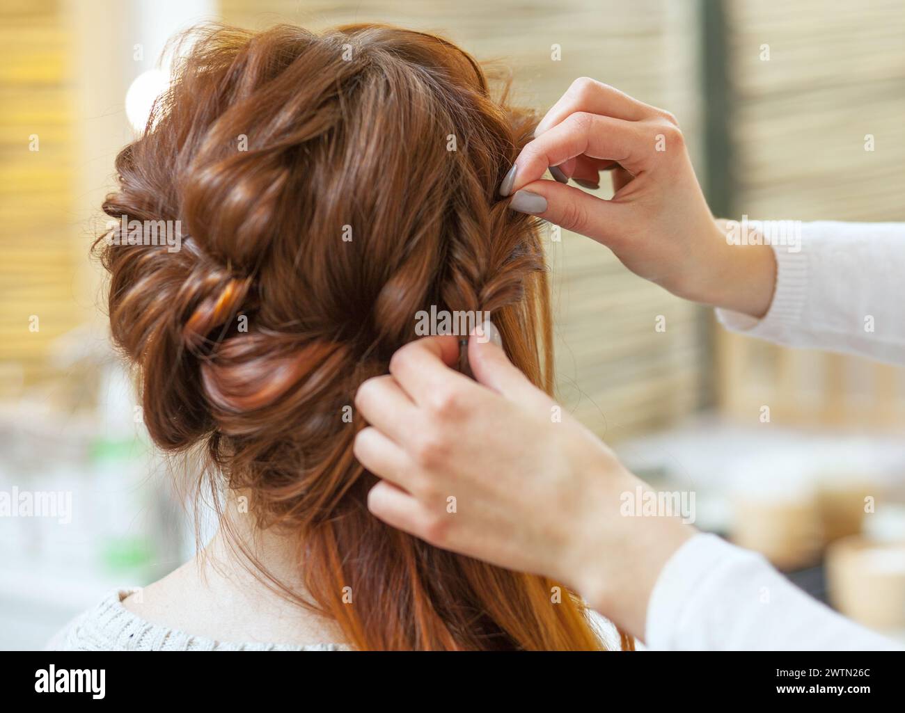 Hermosa chica pelirroja con el pelo largo, peluquería teje una trenza francesa, en un salón de belleza. Cuidado del cabello profesional y crear peinados. Foto de stock