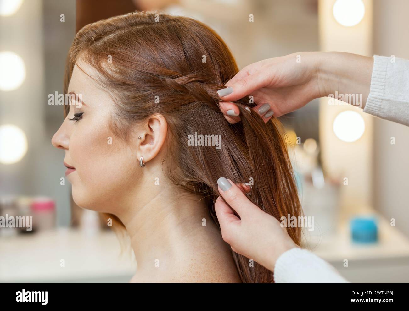 Hermosa chica pelirroja con el pelo largo, peluquería teje una trenza francesa, en un salón de belleza. Cuidado del cabello profesional y crear peinados. Foto de stock