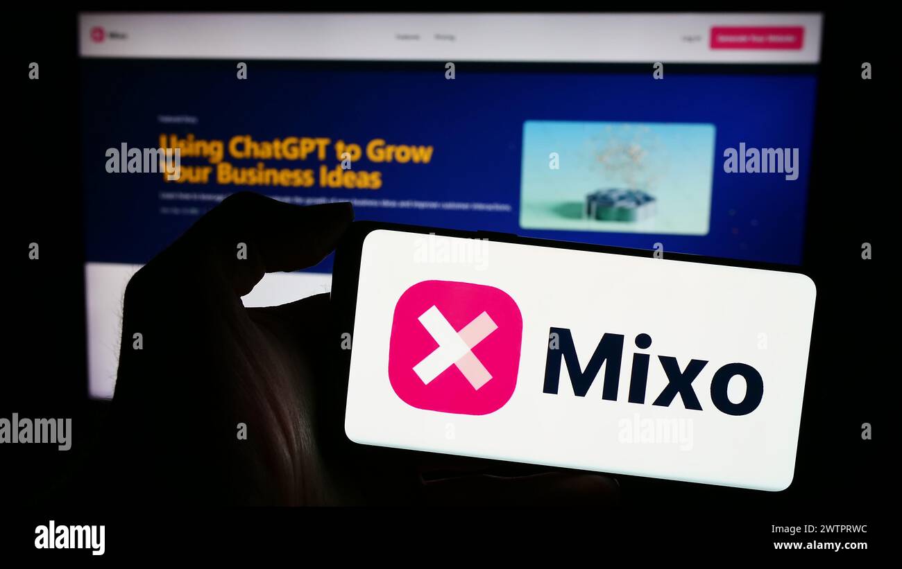Persona que sostiene el teléfono móvil con el logotipo de la empresa de construcción de sitios web de AI Mixo en frente de la página web del negocio. Enfoque en la pantalla del teléfono. Foto de stock