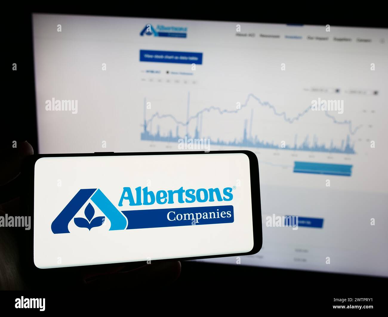 Persona que sostiene el teléfono móvil con el logotipo de la compañía de comestibles al por menor estadounidense Albertsons Companies Inc. Frente a la página web. Enfoque en la pantalla del teléfono. Foto de stock