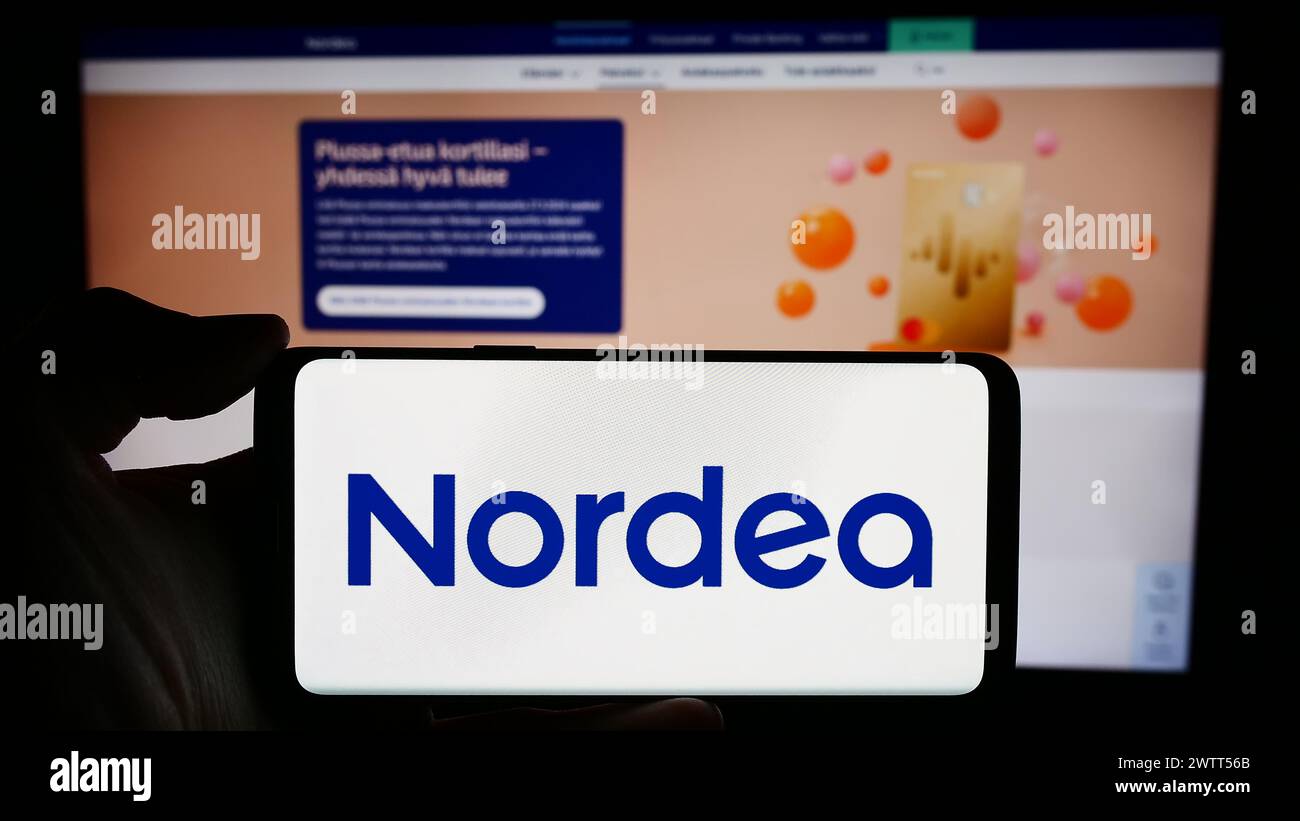 Persona que sostiene el teléfono celular con el logotipo de la compañía finlandesa de servicios financieros Nordea Bank ABP frente a la página web del negocio. Enfoque en la pantalla del teléfono. Foto de stock