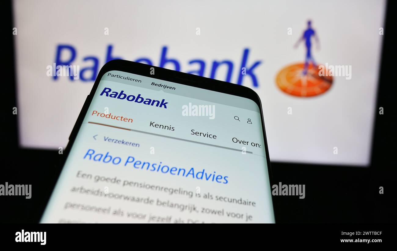 Teléfono móvil con sitio web de la empresa bancaria holandesa Cooperatieve Rabobank U.A. frente al logotipo del negocio. Enfoque en la parte superior izquierda de la pantalla del teléfono. Foto de stock