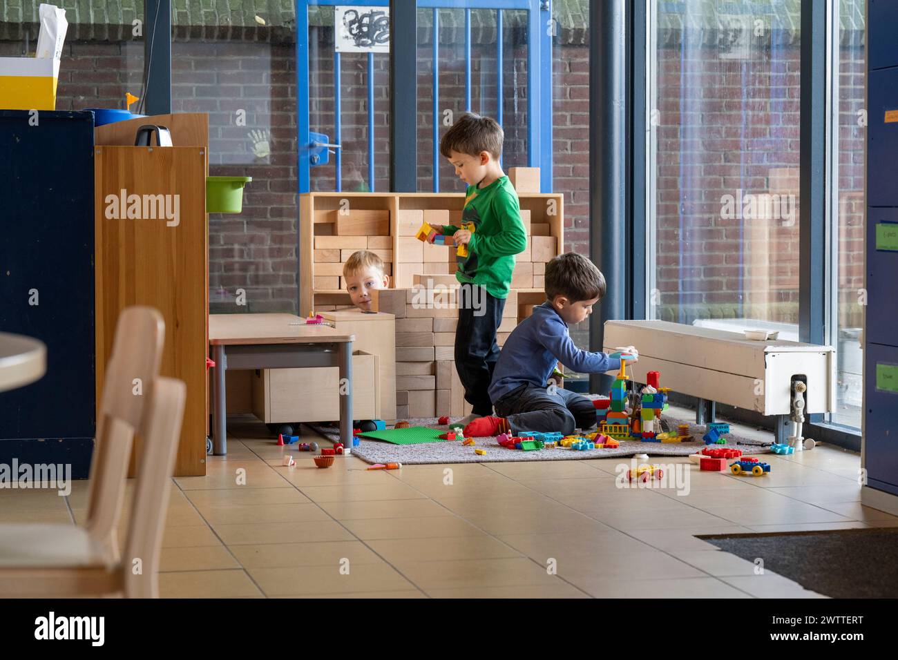 Tres niños jugando con bloques y juguetes en una colorida sala de juegos interior. Foto de stock
