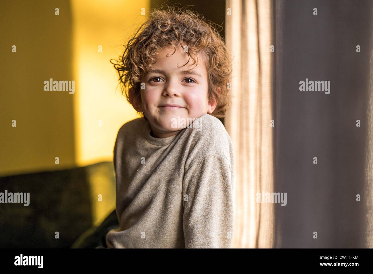 Un niño juguetón mirando desde detrás de una cortina con una sonrisa cálida. Foto de stock