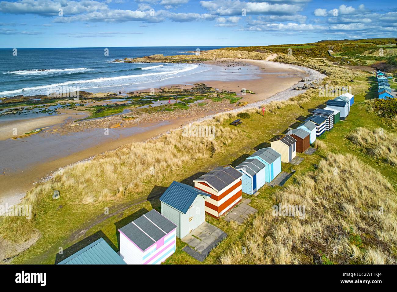 Hopeman Moray Coast Escocia cielo azul y una fila de coloridas cabañas o chalets de playa con vistas a la barrida de la playa de arena Foto de stock