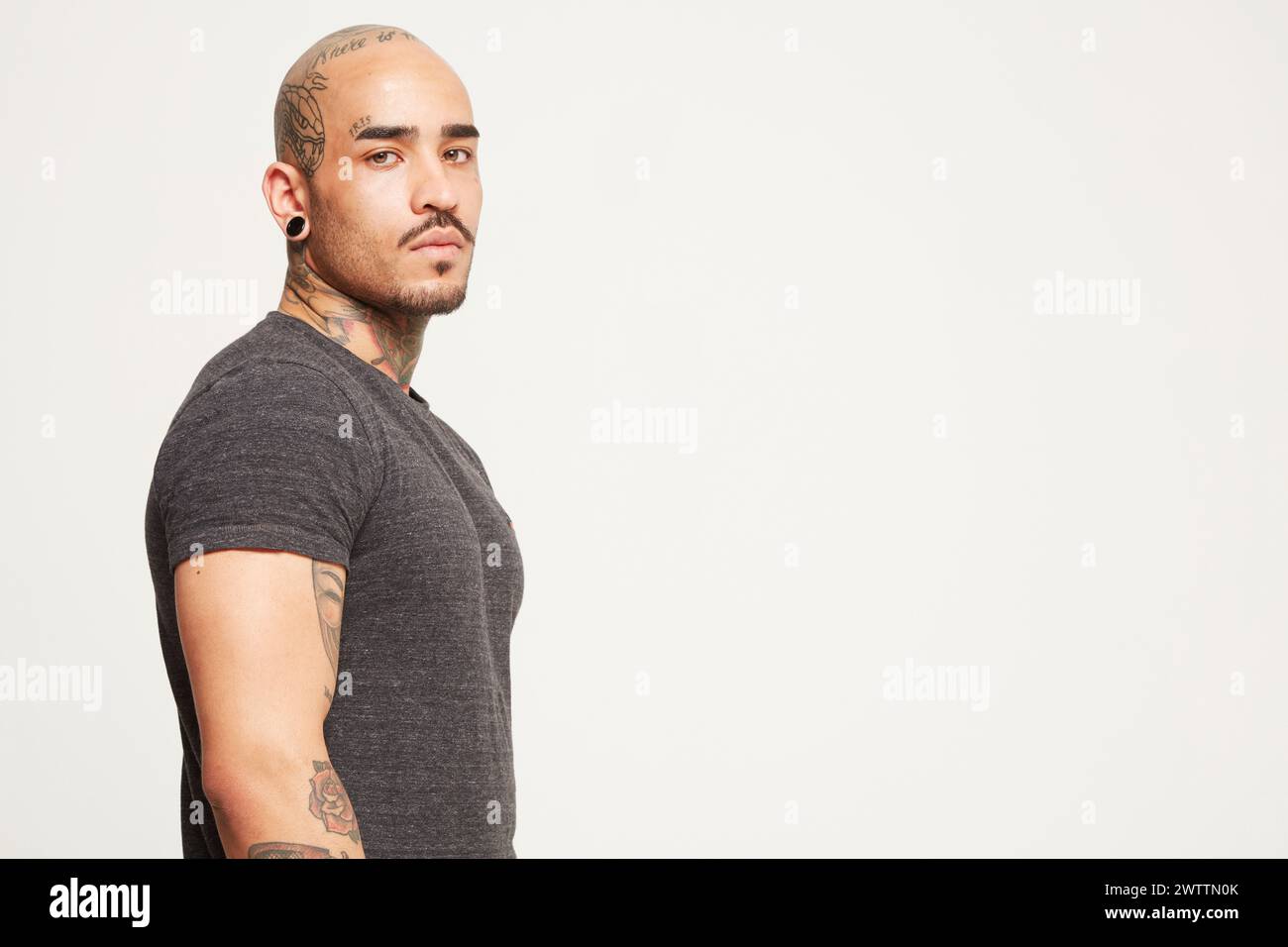 Hombre con tatuajes posando contra un fondo claro Foto de stock