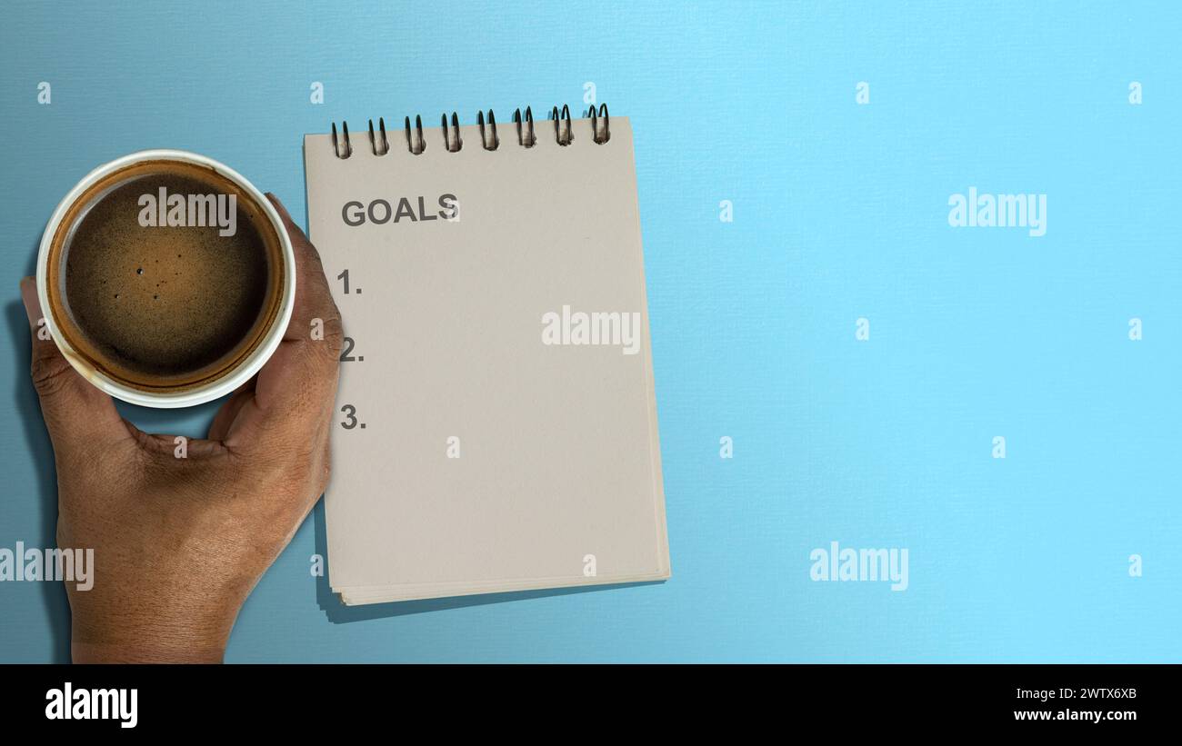 Un cuaderno con texto de lista de objetivos y una taza de café sobre un fondo de color. Planificación y concepto de objetivo Foto de stock