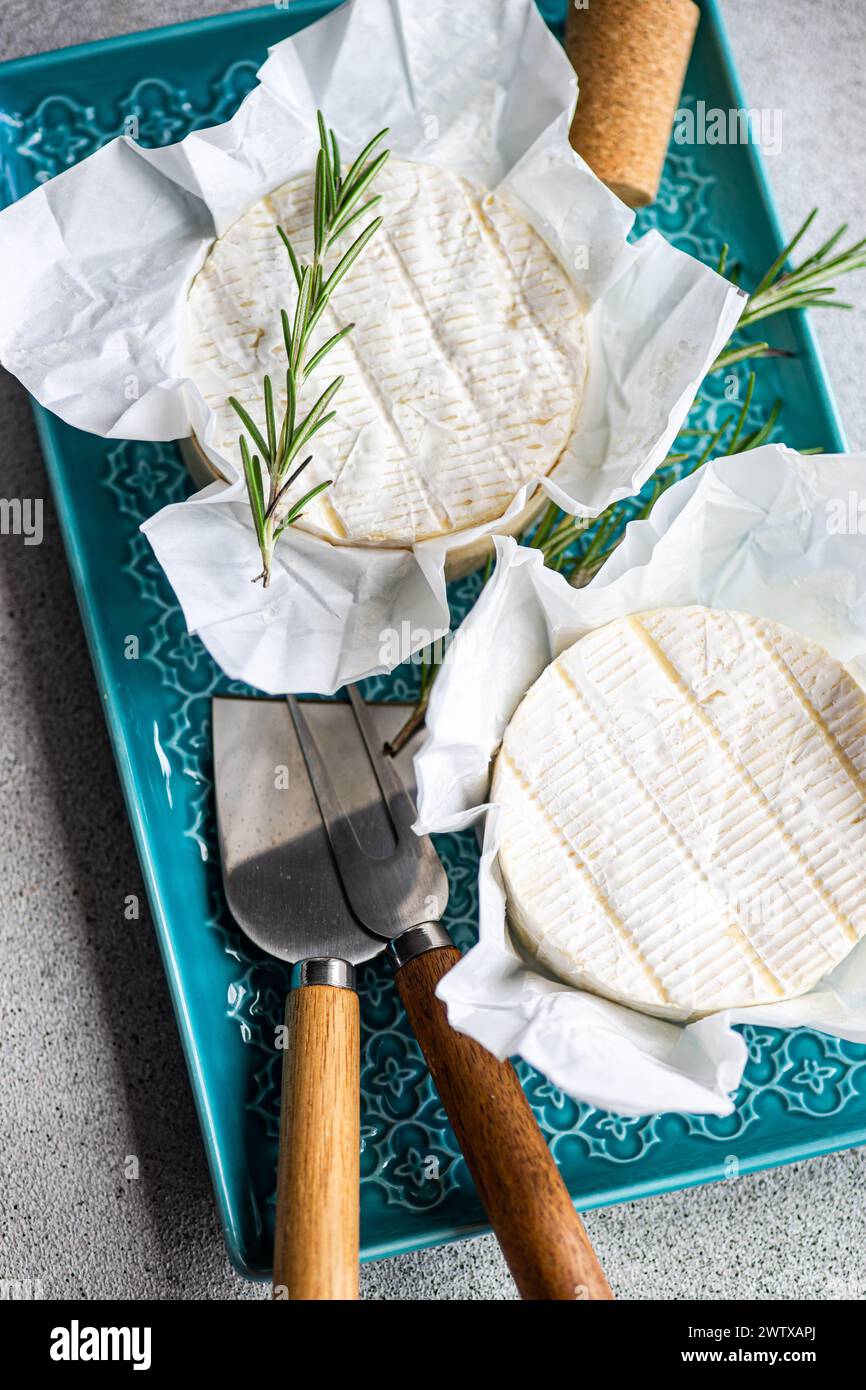 Vista aérea de todo un brie con romero fresco en un plato con cuchillos de queso Foto de stock