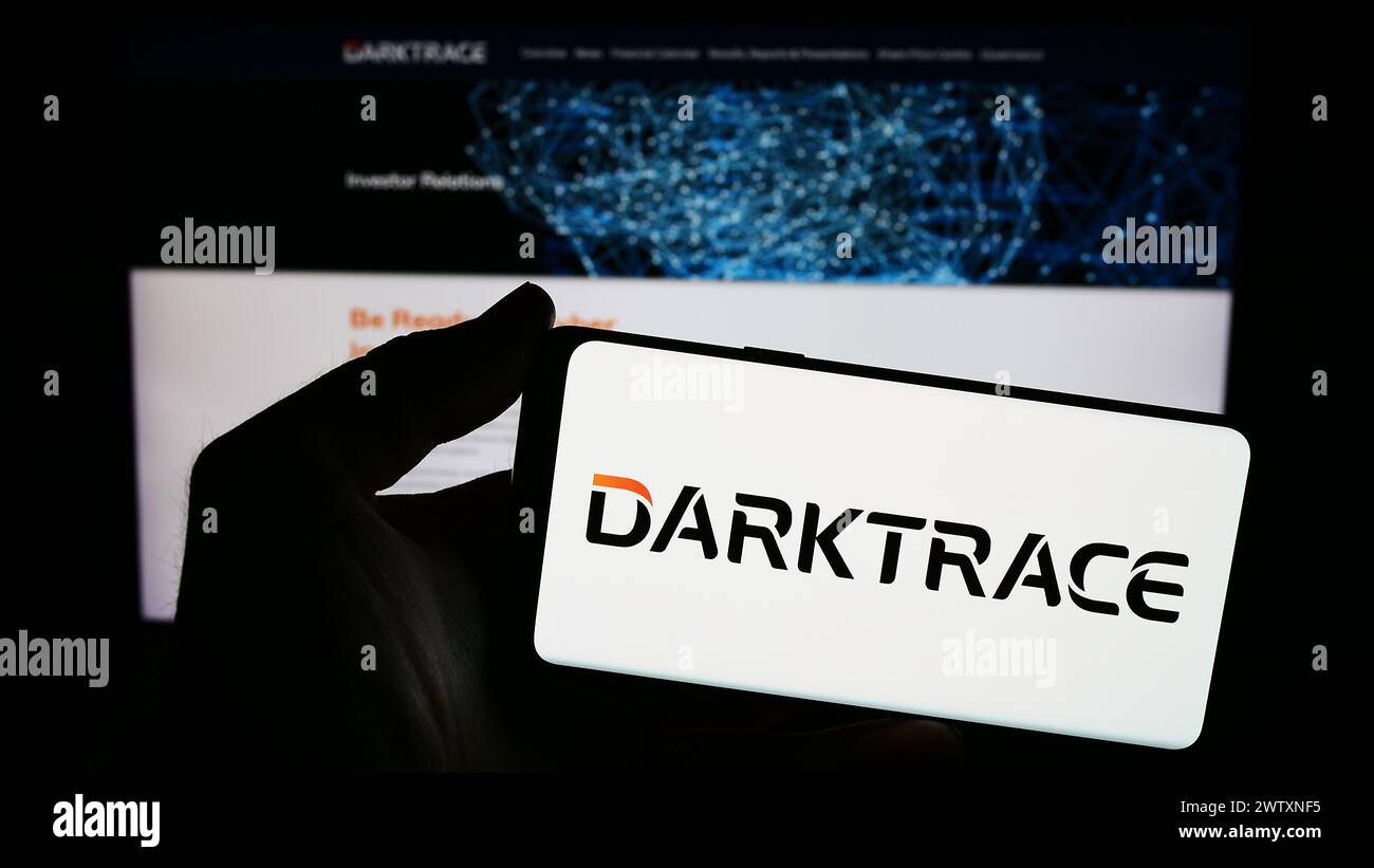 Persona que sostiene el smartphone con el logotipo de la compañía británica de seguridad cibernética Darktrace plc en frente del sitio web. Enfoque en la pantalla del teléfono. Foto de stock