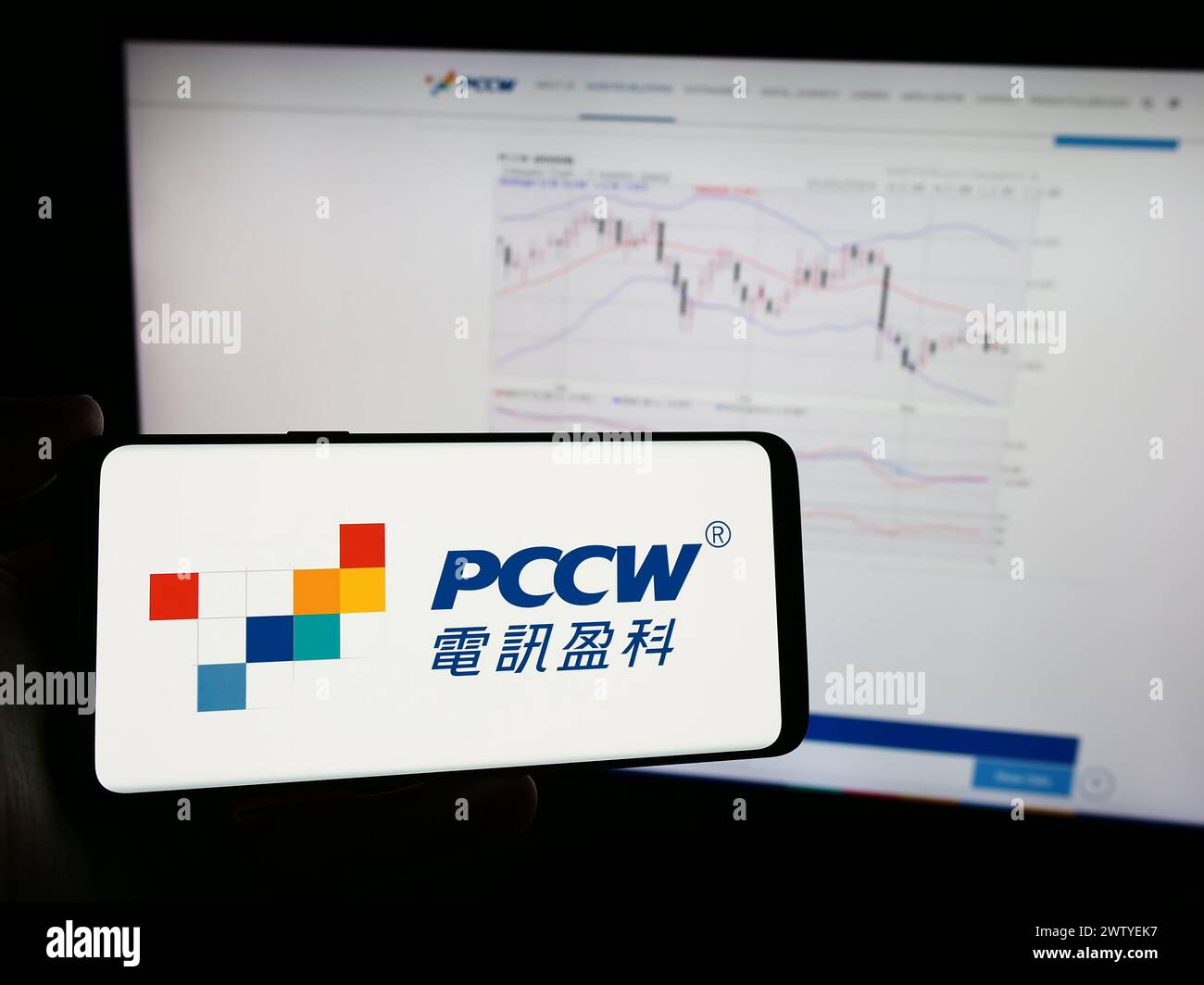 Persona que sostiene el teléfono móvil con el logotipo de la compañía de telecomunicaciones PCCW Limited delante de la página web del negocio. Enfoque en la pantalla del teléfono. Foto de stock