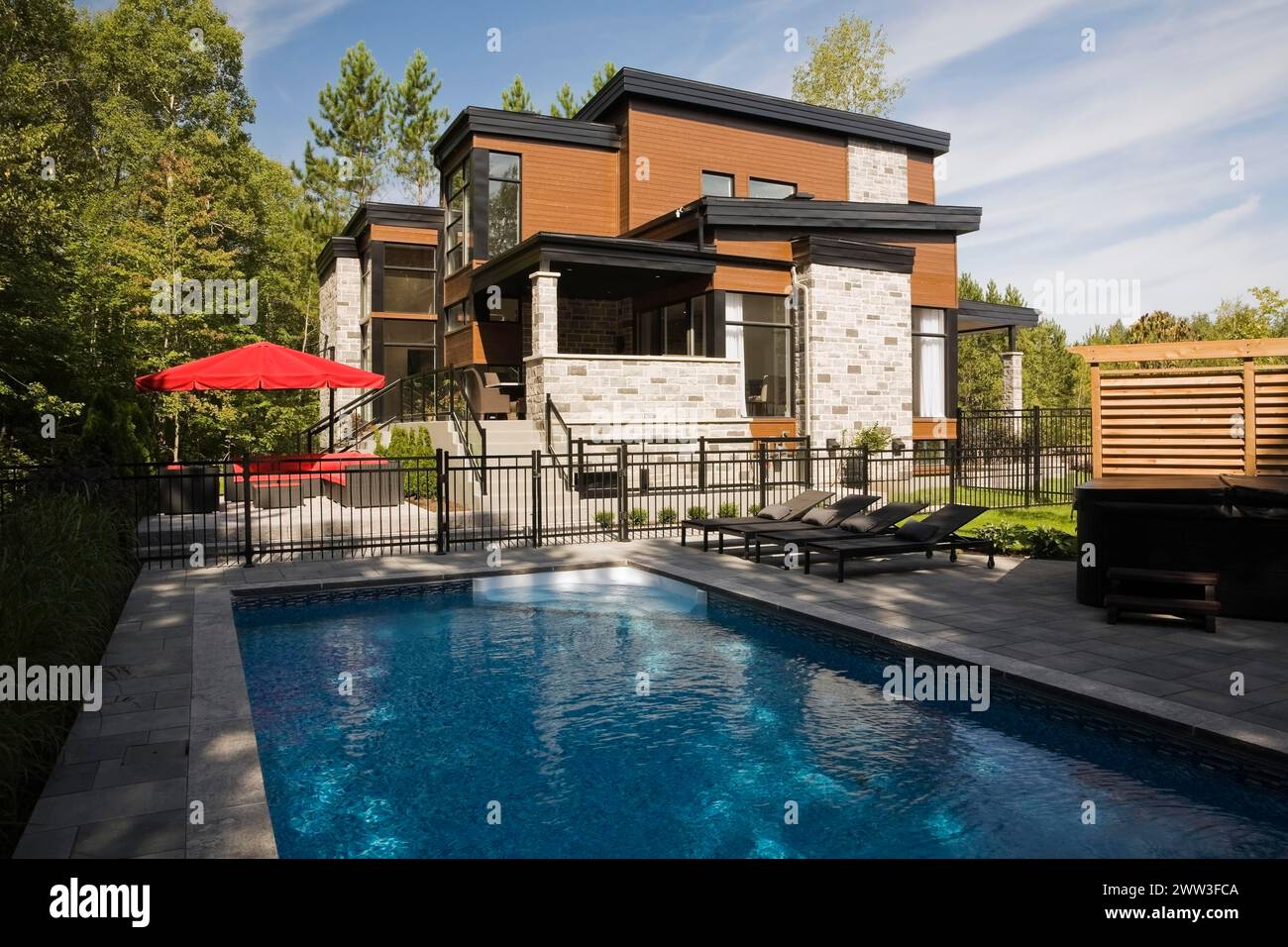 Dos pisos gris, beige y piedra cortada tan con revestimiento de madera y adornos negros casa y piscina interior en verano, Quebec, Canadá Foto de stock