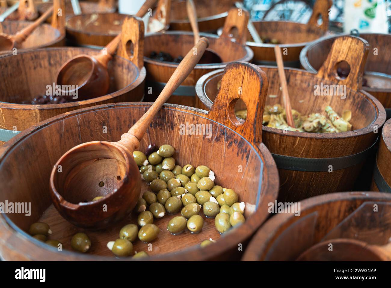 Primer plano de aceitunas verdes en cuencos de madera con palas en un puesto del mercado Foto de stock