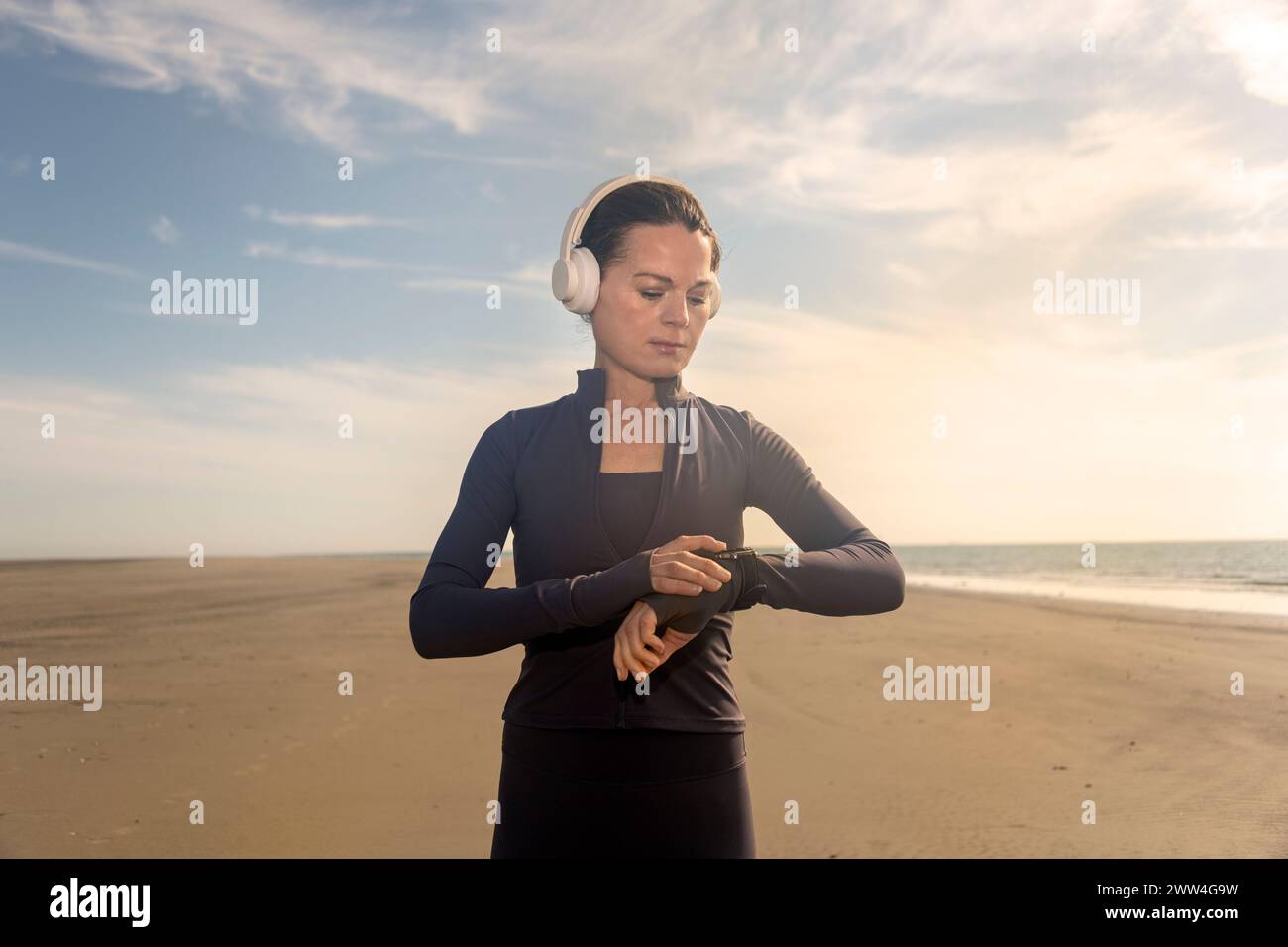 Mujer revisando su reloj inteligente para el pulso y la actividad, correr y hacer ejercicio en la playa Foto de stock