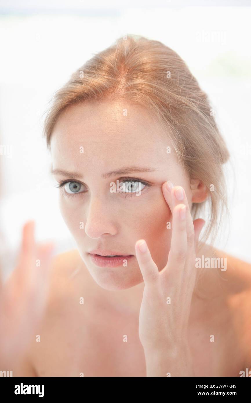 Interesados mujer mirando en el espejo comprobando su cara Foto de stock