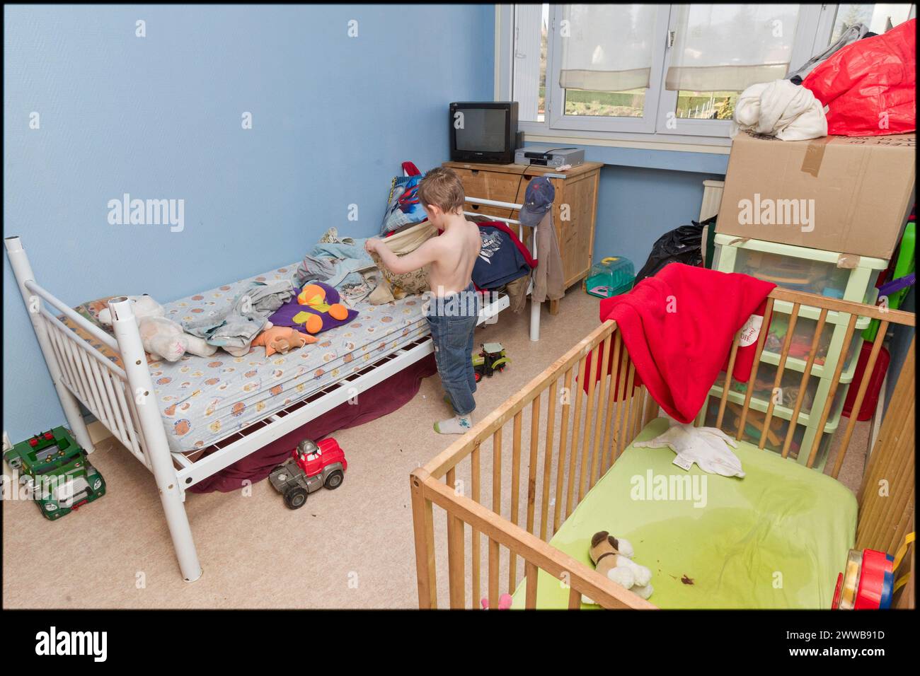 ASE - Asistencia Social a la Infancia. Morgan, de 5 años, se viste solo como un adulto en su habitación donde duerme con su hermano pequeño Maxence. Foto de stock