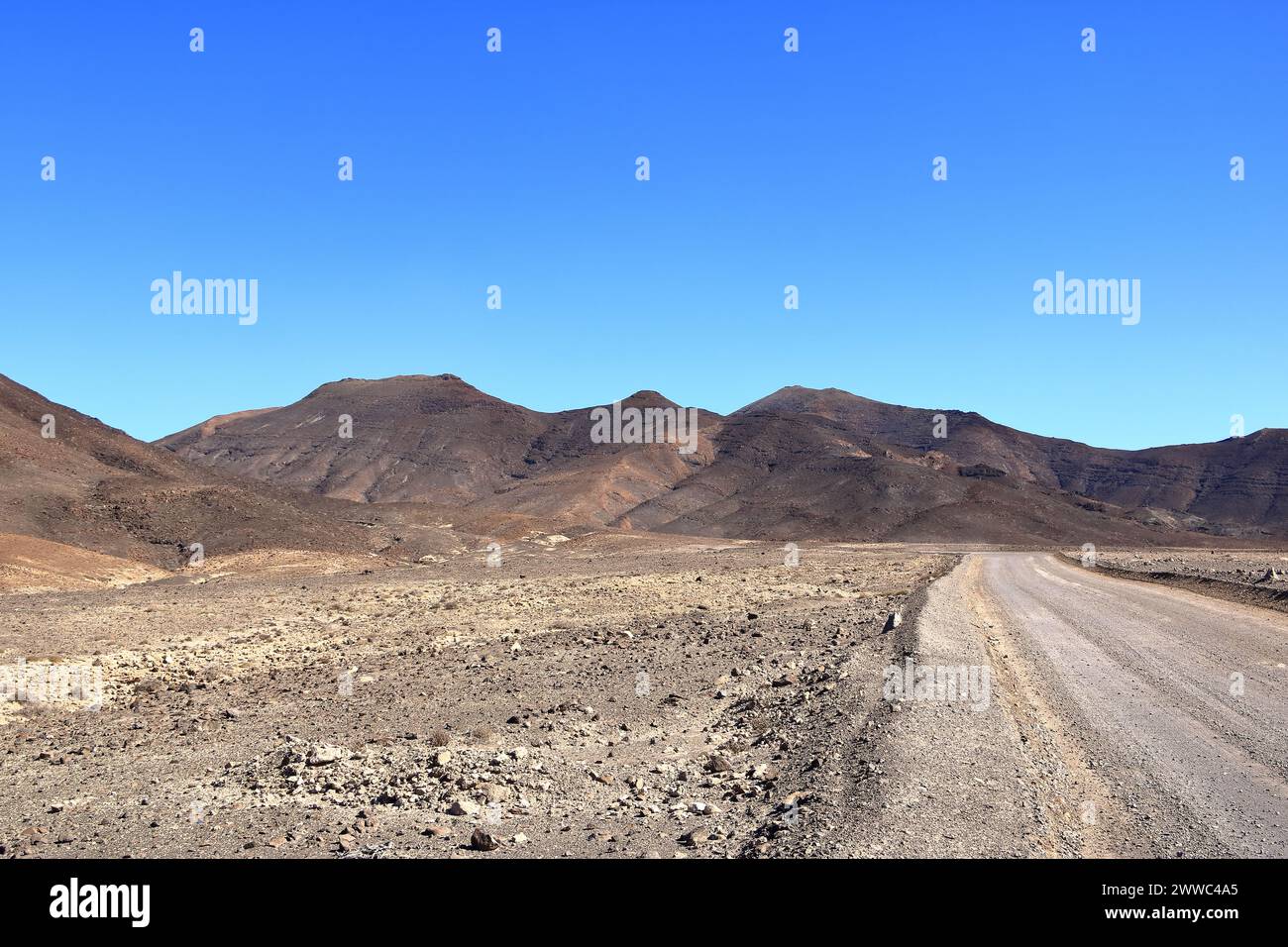 Grava, camino polvoriento con altas montañas volcánicas en el fondo. Jandia, Morro Jable, Fuerteventura, Islas Canarias en España Foto de stock