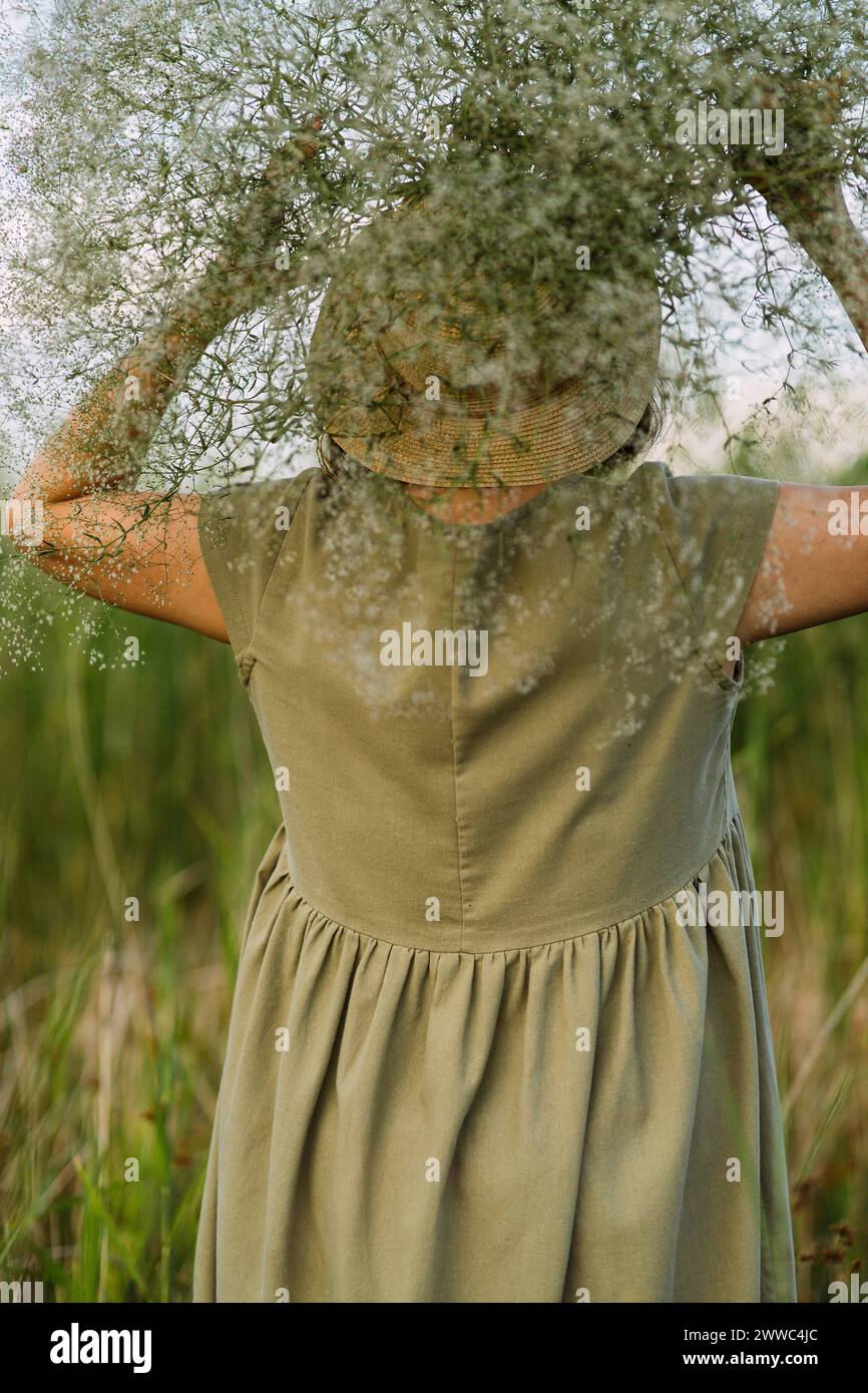 Mujer madura que lleva flores de gypsophila sobre la cabeza en el campo Foto de stock