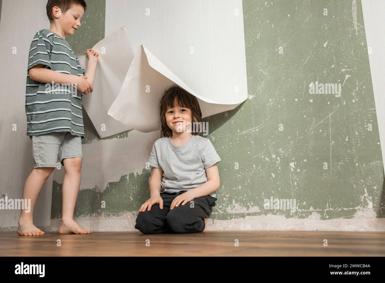 Hermanos jugando con el papel pintado renovando casa Foto de stock