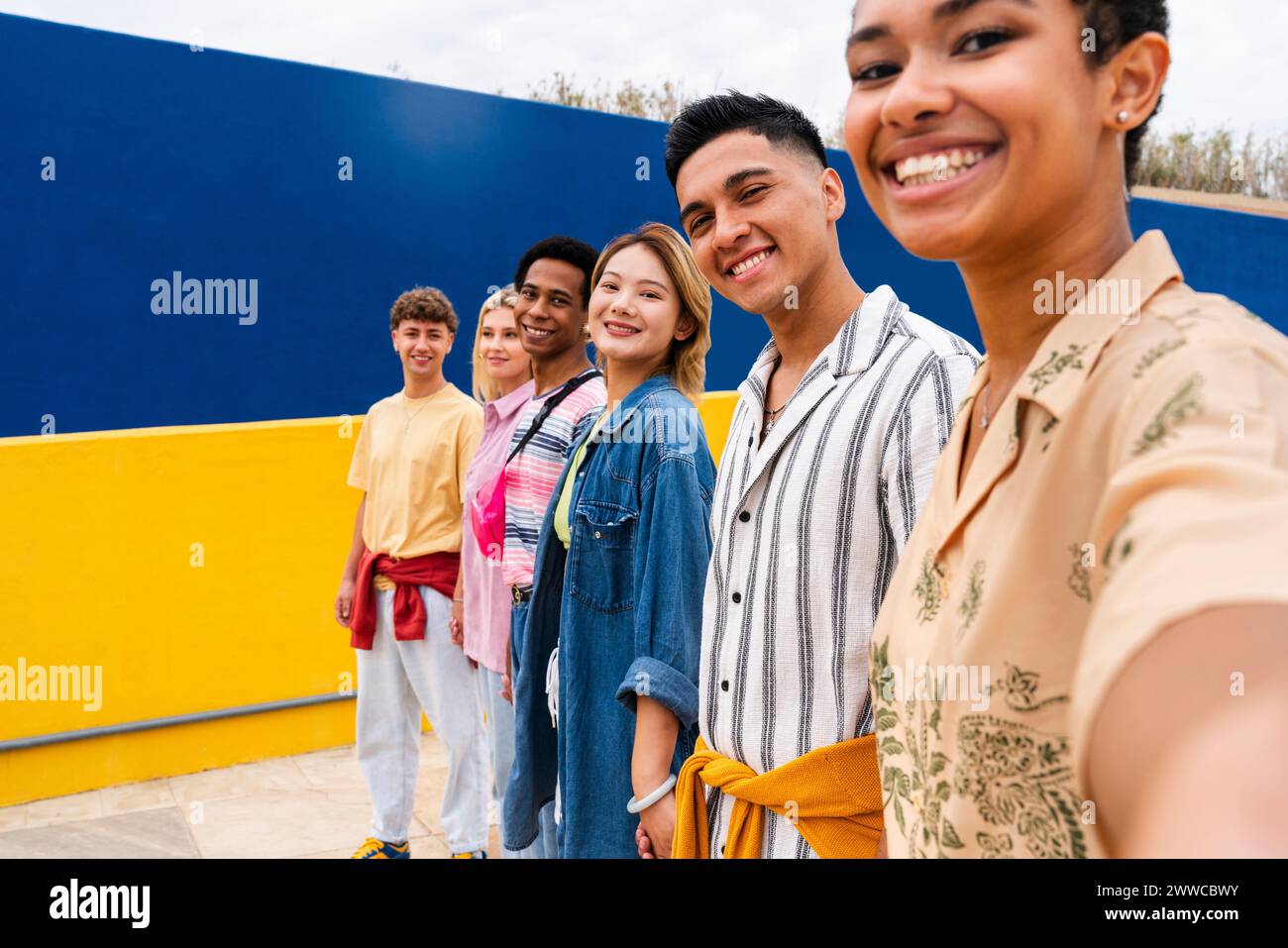 Grupo multiétnico de jóvenes amigos de pie sonriendo frente a la pared colorida Foto de stock