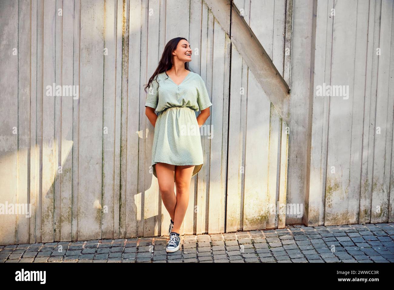 Sonriente mujer joven apoyada en la pared Foto de stock