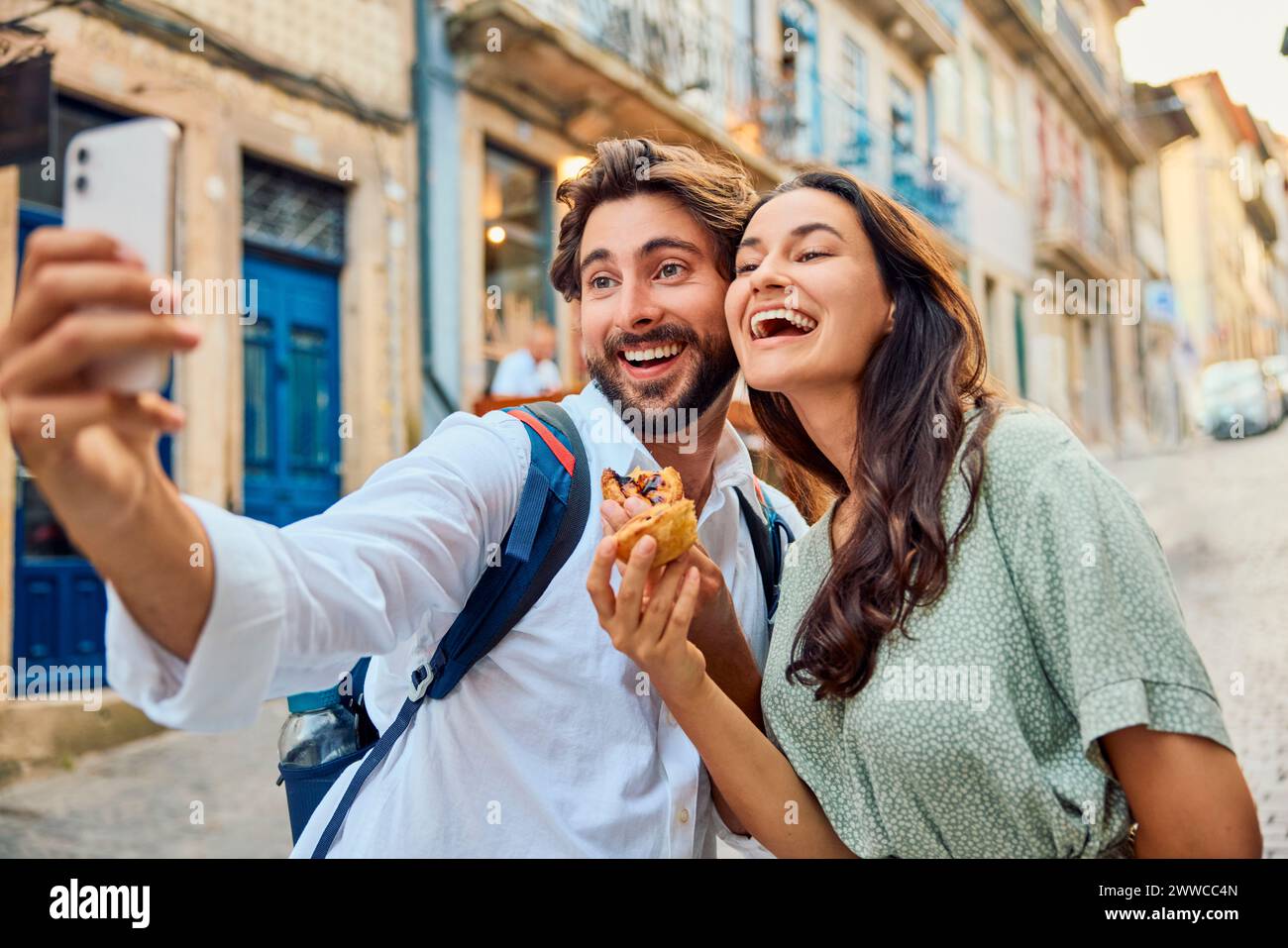 Alegre pareja sosteniendo el tradicional postre pastel de nata y tomando selfie a través de teléfono inteligente Foto de stock