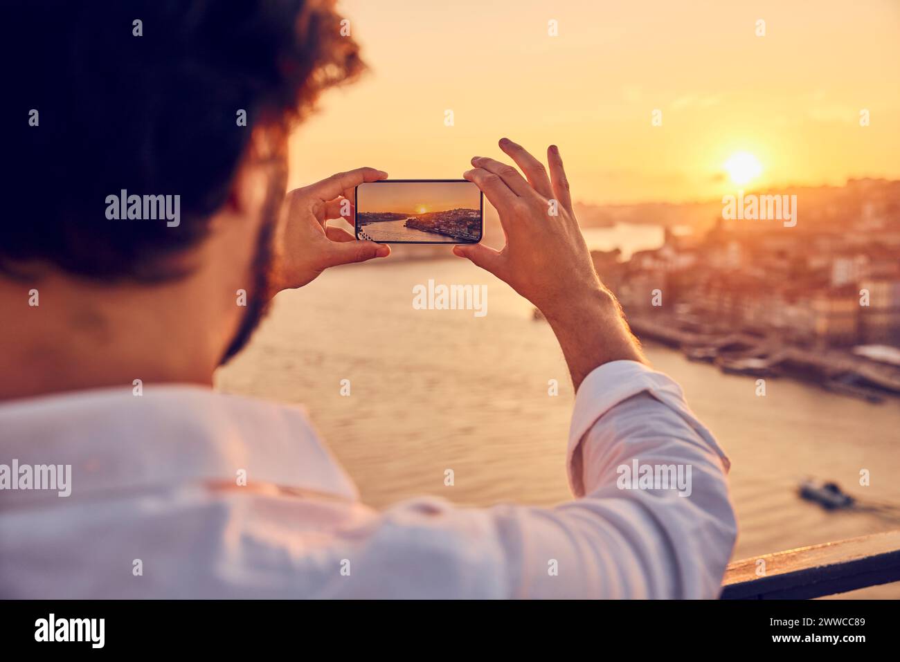 Hombre fotografiando la ciudad de Oporto a través de teléfono inteligente al atardecer en Portugal Foto de stock